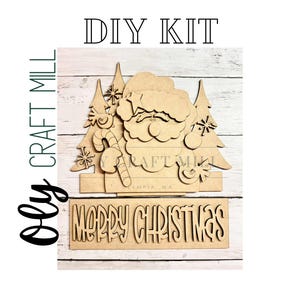 May include: A DIY kit featuring a wooden Santa Claus design with trees and candy canes. The words "DIY KIT" and "MERRY CHRISTMAS" are included in the design. The Oly Craft Mill logo is on the left side.