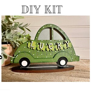 May include: DIY craft kit featuring a green wooden car with white wheels and the word "LUCKY" spelled out in shamrock letters. The car is decorated with white polka dots and shamrocks.