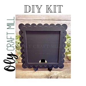 May include: DIY kit for a black scalloped frame with a cutout in the center. The frame is on a wooden stand. The text "DIY KIT" is at the top of the image and "Olly Craft Mill" is on the left side of the image.