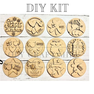 May include: A DIY kit featuring twelve wooden circles with various laser-cut designs and text. Designs include snowflakes, hearts, shamrocks, a house, and a star with the words "Let it Snow", "Love", "Irish", "Hello", "Summer", and "Simply Blessed".