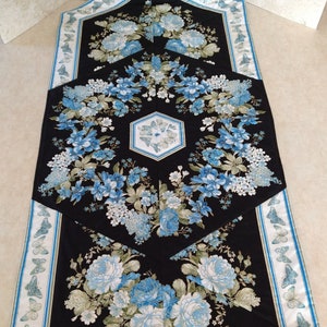 May include: A black table runner with a hexagonal design featuring blue and white floral patterns and a border of blue butterflies.
