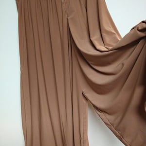May include: A pair of wide-legged pants in a light brown color. The pants have a loose, flowing fit and a wide waistband.