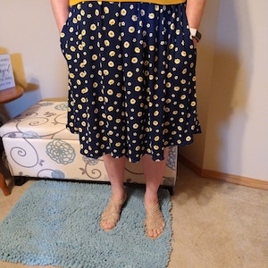 May include: A navy blue skirt with a yellow daisy print. The skirt has pockets on the sides and is knee-length.