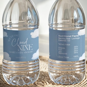 May include: Two clear plastic water bottles with white caps and blue labels. The labels read "Cloud Nine" and "baby shower". One label includes a nutritional facts table. The bottles sit on a woven mat.
