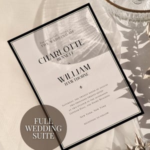 May include: Elegant wedding invitation with black border, featuring the names Charlotte Bennett and William Hawthorne. The invitation includes event details and is part of a full wedding suite. Decorative elements include a glass serving dish and silver foliage.
