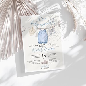 May include: A blue baby shower invitation with a watercolor illustration of a baby's outfit hanging on a clothesline. The invitation reads "It's a baby sprinkle!" and includes the name "Nichol Woods", the date "Sept 15, 2025", and the time "At 2pm".