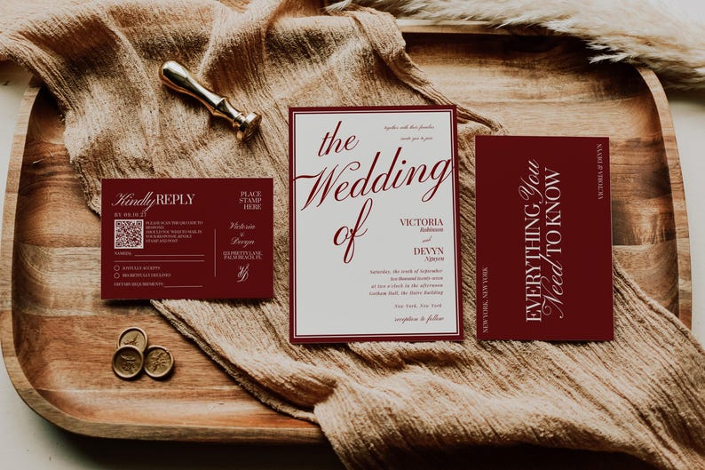 May include: A wedding invitation suite featuring a burgundy and cream color scheme. The suite includes an invitation, RSVP card, and details card. Gold wax seals and a gold pen are also present on a wooden tray.