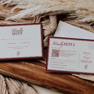 May include: Two wedding reply cards with burgundy borders and text, including "Kindly Reply" and a QR code. One card is next to a white envelope, all on a wooden surface with a beige fabric background.