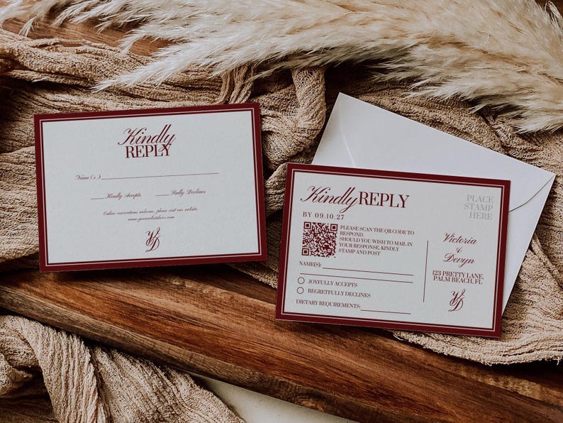 May include: Two wedding reply cards with burgundy borders and text, including "Kindly Reply" and a QR code. One card is next to a white envelope, all on a wooden surface with a beige fabric background.