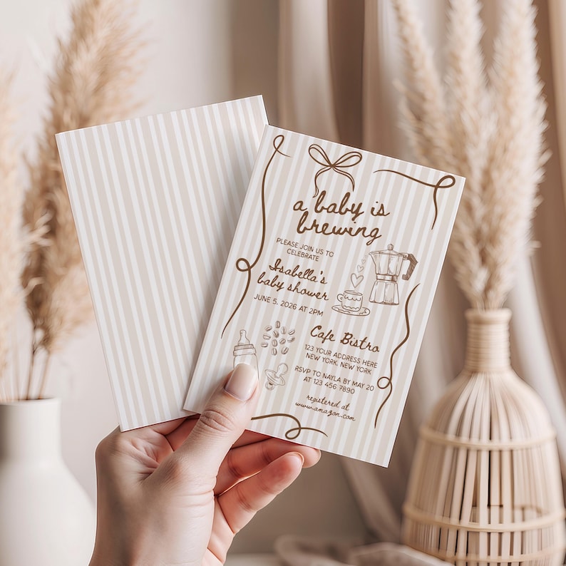 May include: Baby shower invitation with the text "a baby is brewing" and "Isabella's baby shower". The invitation has a striped background and features illustrations of a coffee pot, coffee cup, and baby bottle. The invitation is held in a person's hand.