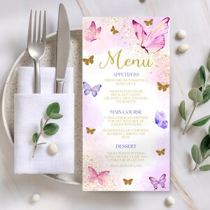 May include: A menu card with a butterfly theme. The menu features a pink and gold color scheme with butterfly illustrations. The menu includes appetizers, main course, and dessert options. A fork, knife, and napkin are on a plate to the left.