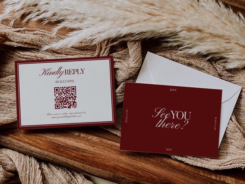 May include: Burgundy and white wedding invitation suite. The invitation card reads "Kindly Reply" with a QR code and date. The RSVP card says "See you there?" with a white envelope on a wooden surface.