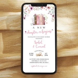 May include: A smartphone displays a baby shower invitation. The design features floral accents, a stack of books, and the text "A New Chapter Begins." The invitation is for Isabel & Conrad, with the date, time, and location details.