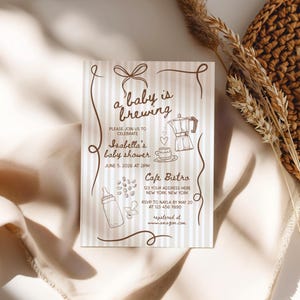 May include: A baby shower invitation with a striped background and brown illustrations of a coffee pot, baby bottle, and pacifier. The text reads "a baby is brewing" and includes details for Isabella's baby shower at Cafe Bistro.