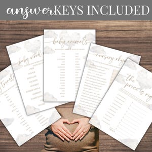 May include: A collection of baby shower game cards with cloud and gold accents, including "Baby Word," "Baby Animals," and "Nursery Rhymes." The text "ANSWER KEYS INCLUDED" is at the top. The cards are arranged on a wooden surface.