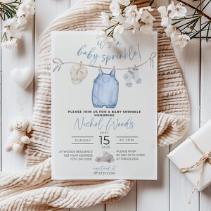 May include: A blue baby shower invitation with a watercolor illustration of a baby's overalls, hat, and socks hanging on a clothesline. The text reads "It's a baby sprinkle!" and includes the name "Nichol Woods", the date "Sept 15, 2025", and the time "at 2pm".