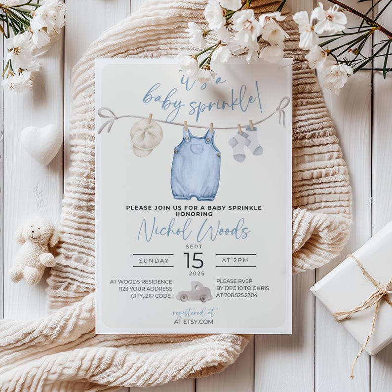 May include: A blue baby shower invitation with a watercolor illustration of a baby's overalls, hat, and socks hanging on a clothesline. The text reads "It's a baby sprinkle!" and includes the name "Nichol Woods", the date "Sept 15, 2025", and the time "at 2pm".