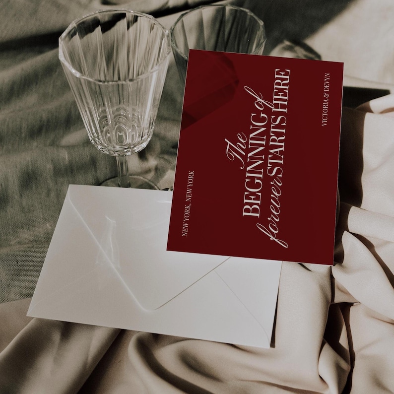 May include: A burgundy invitation card with the text "The Beginning of forever STARTS HERE" and the names Victoria & Devyn. A white envelope and two clear wine glasses are also in the image. The text "NEW YORK, NEW YORK" is at the bottom.