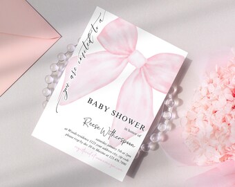 May include: A white rectangular invitation card featuring a large, soft pink watercolor bow graphic at the top. The text reads: You are invited to a BABY SHOWER in honor of Reese Witherspoon, saturday january 5th at 2pm at Woods residence 1123.