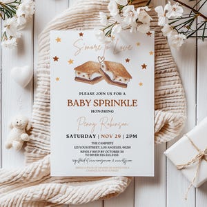 Könnte beinhalten: Eine weiße Babyparty-Einladung mit einer braunen und weißen Illustration von zwei Marshmallow-Brötchen. Die Einladung lautet "S'more to Love" und enthält den Text "Baby Sprinkle" zu Ehren von "Penny Robinson". Die Veranstaltung findet am Samstag, den 29. November um 14:00 Uhr im Campsite, 123 Your Street, Los Angeles, 90210 statt. Bitte melden Sie sich bis zum 30. Oktober bei River 555.555.5555 an. Die Einladung enthält auch den Text "registriert bei www.amazon.com & www.target.com" und "Bringen Sie eine Packung Windeln oder Feuchttücher mit, um die Chance auf einen Preis zu gewinnen!"