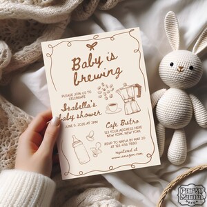 Puede incluir: Una invitaci&oacute;n de baby shower beige con texto e ilustraciones marrones. El texto dice "Baby is brewing" e "Isabella's baby shower". La invitaci&oacute;n incluye detalles sobre la fecha, la hora, el lugar y la informaci&oacute;n de RSVP.