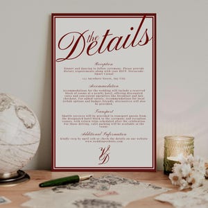 May include: A wedding details card with a burgundy border and text. The card includes information about the reception, accommodation, and transport. A globe, pen, and candle are in the background.