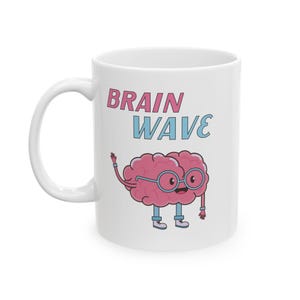 May include: White ceramic mug with the words "BRAIN WAVE" in pink and blue. The mug features a cartoon brain character wearing glasses and shoes. The brain is pink with blue accents.