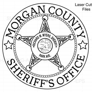 May include: Black and white illustration of a sheriff's badge with the words "Morgan County Sheriff's Office" around the perimeter. The badge features a five-pointed star with a smaller circle in the center that reads "Richard W. Myers, Sheriff, Park Ave."