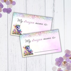 May include: Two printable cards featuring a purple dragon illustration and the text "My dragon name is:" on each card. The cards have a pink and purple watercolour background with glitter.