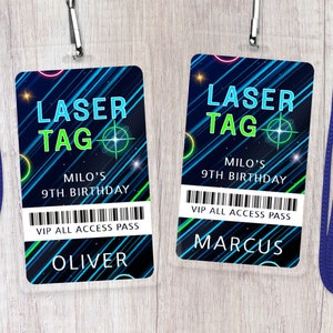 May include: Two blue and green laser tag party favour badges with a black background and white text. The text on the badges reads "Laser Tag", "Milo's 9th Birthday", and "VIP All Access Pass". One badge says "Oliver" and the other says "Marcus".