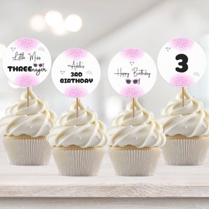 May include: Four cupcakes with pink and white frosting and decorative toppers. The toppers feature pink and white polka dots and text that says "Little Miss Three-nager", "Adele's 3rd Birthday", "Happy Birthday", and "3".