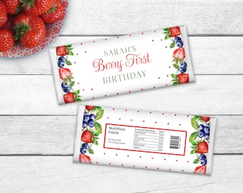 May include: A white chocolate bar wrapper with red polka dots and a border of strawberries and blueberries. The wrapper says "SARAH'S Berry First BIRTHDAY". The back of the wrapper has a nutrition facts label with a list of ingredients and their percentage daily value.