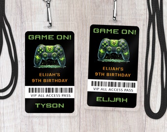 May include: Two black and green plastic VIP all access passes with a green and black video game controller graphic. The text "GAME ON!" is at the top of each pass. The text "ELIJAH'S 9TH BIRTHDAY" is below the graphic. The text "VIP ALL ACCESS PASS" is below the birthday text. The name "TYSON" is on the left pass and the name "ELIJAH" is on the right pass.