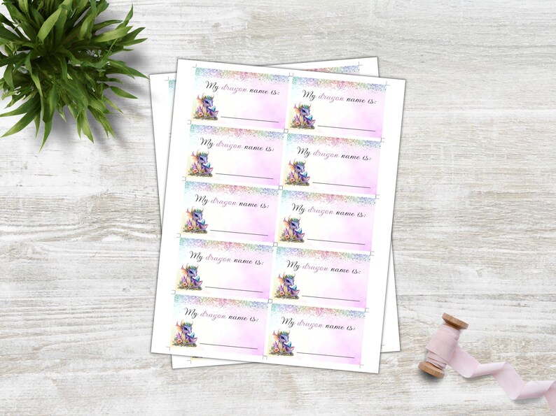 May include: Ten printable name tags featuring a cute cartoon dragon with rainbow wings and a pink background. The text on each tag reads "My dragon name is".