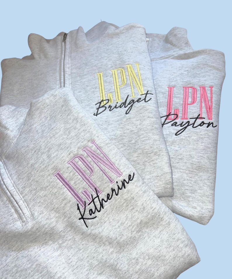 May include: Three gray sweatshirts with a zipper. The sweatshirts have the letters 'LPN' embroidered on them in different colors. The first sweatshirt has yellow embroidery and the name 'Bridget' written underneath. The second sweatshirt has pink embroidery and the name 'Payton' written underneath. The third sweatshirt has purple embroidery and the name 'Katherine' written underneath.