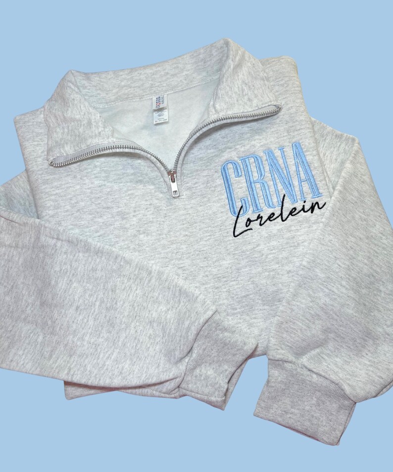 May include: Gray sweatshirt with a blue embroidered design that says "CRNA Lorelei"