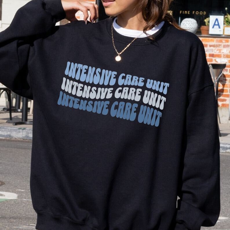 Peut inclure: Sweat-shirt noir avec le texte "INTENSIVE CARE UNIT" r&eacute;p&eacute;t&eacute; trois fois dans un d&eacute;grad&eacute; bleu et blanc, chaque mot dans une police r&eacute;tro et ondul&eacute;e.
