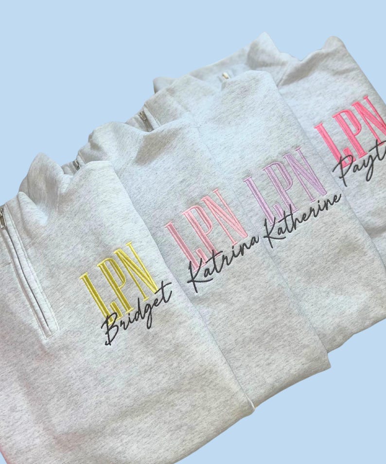 May include: Several light gray quarter-zip sweatshirts with embroidered text. Each sweatshirt has "LPN" in a different color, with a name below. The colors include yellow, pink, and purple. The background is a light blue.
