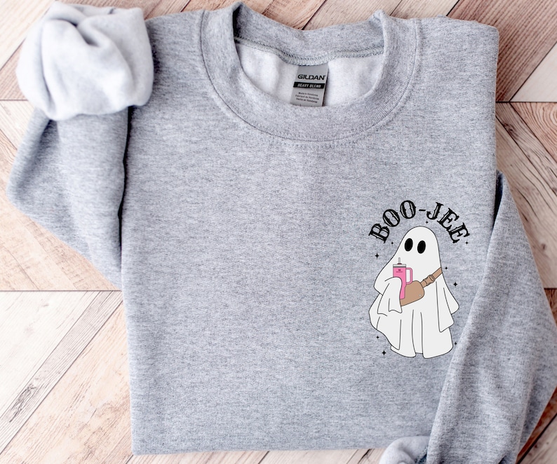 May include: A heather gray sweatshirt featuring a cartoon ghost with the text "Boo-jee". The ghost is holding a pink drink and wearing a brown fanny pack. The design includes small star accents.