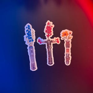May include: Three light saber stickers with different coloured flowers in the hilt. The flowers are blue, red and yellow.