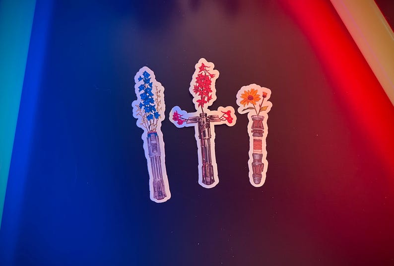 May include: Three light saber stickers with different coloured flowers in the hilt. The flowers are blue, red and yellow.