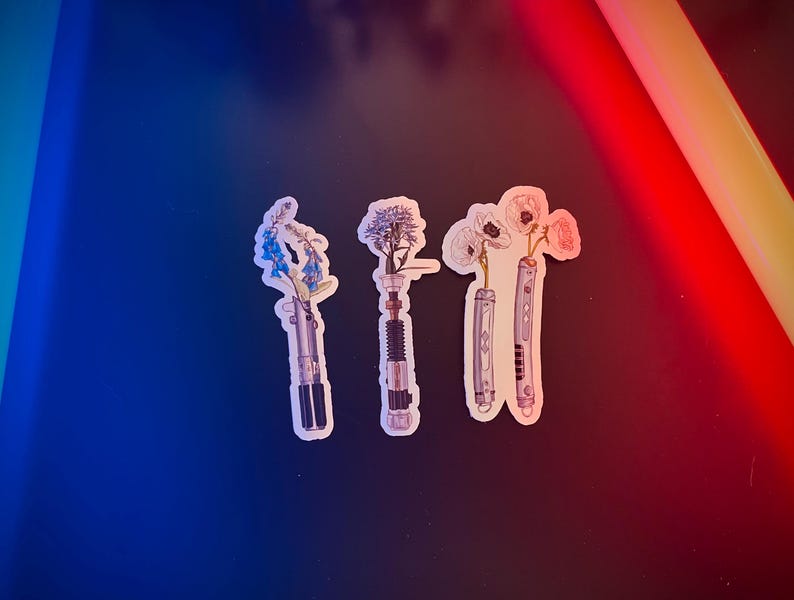 May include: Four stickers featuring different flowers in a lightsaber design. The flowers are blue, white, and pink. The lightsabers are silver and black.