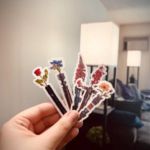 May include: Six different flower stickers with a lightsaber design. The flowers are a red rose, blue and white flowers, two red flowers, and a yellow sunflower.