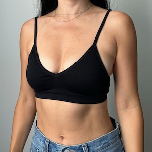 May include: A black seamless bralette with a V-neckline and adjustable straps. The bralette is made of a soft, stretchy fabric and is perfect for layering or wearing on its own.