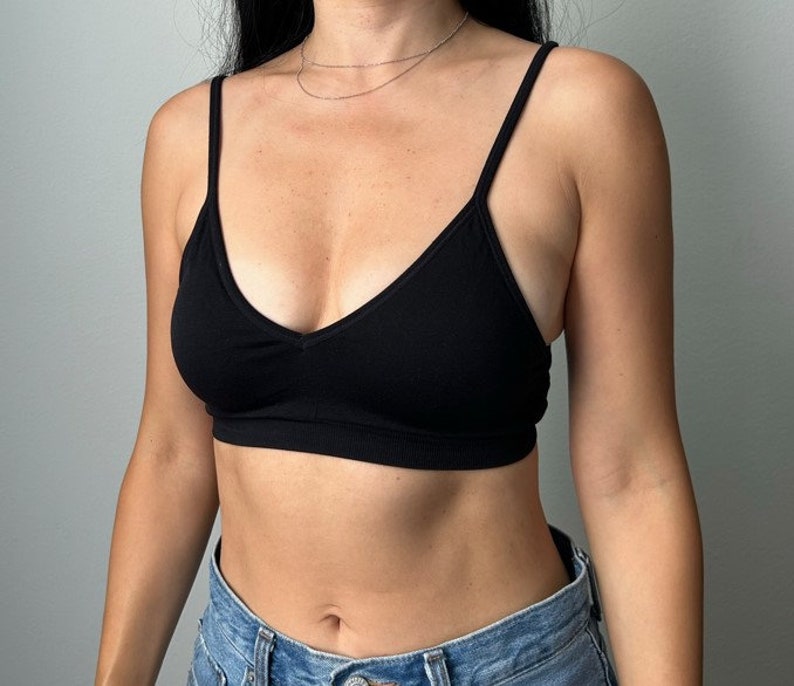 May include: A black seamless bralette with a V-neckline and adjustable straps. The bralette is made of a soft, stretchy fabric and is perfect for layering or wearing on its own.