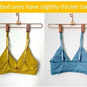 May include: Two bras hanging on a gold hanger. The bra on the left is a solid mustard yellow color. The bra on the right is a ribbed light blue color. The text "Ribbed ones have slightly thicker backs" is at the top of the image.