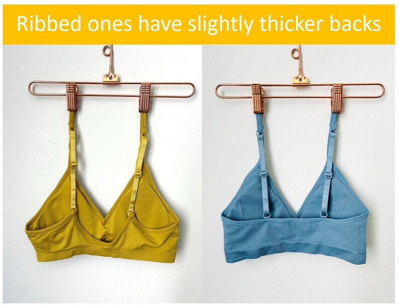 May include: Two bras hanging on a gold hanger. The bra on the left is a solid mustard yellow color. The bra on the right is a ribbed light blue color. The text "Ribbed ones have slightly thicker backs" is at the top of the image.
