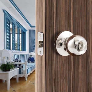 Puede incluir: Un pomo de puerta plateado con una manija redonda y una placa de cierre cuadrada. El pomo está montado en una puerta de madera.