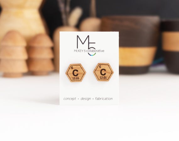 Tiny periodic table elements laser-cut from real wood and mounted on hypoallergenic titanium posts — wearable chemistry that's actually handmade.