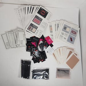 May include: A collection of Mary Kay cosmetic samples including numerous paper product information cards, small black foil sachets, two clear plastic bags filled with black disposable mascara wands, and a small rectangular box labeled 75.